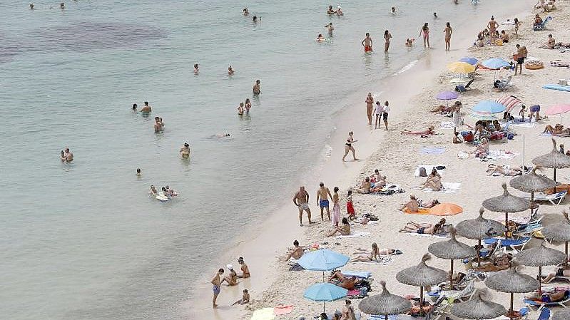 Touristen genießen an einem Strand bei Puerto Portals auf Mallorca die Sonne und das Meer. Foto: Clara Margais/dpa