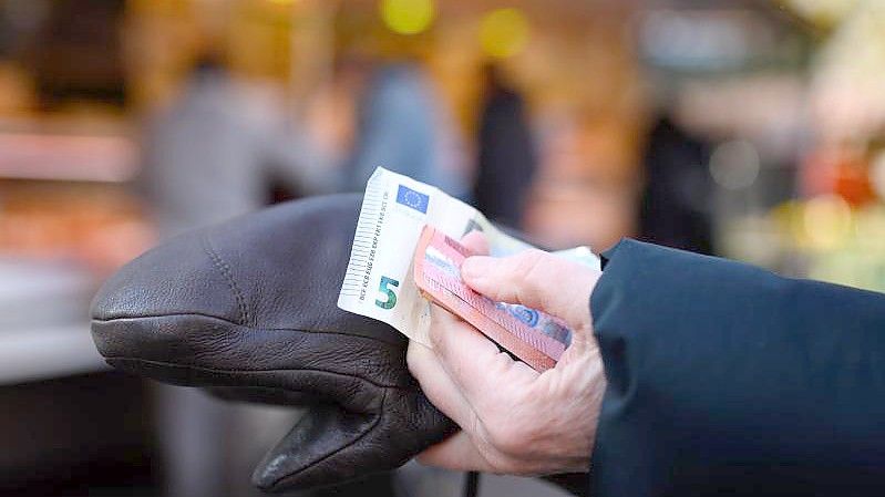 Eine Frau steht an einem Marktstand und hält das Bargeld für ihren Einkauf bereit. Foto: Jonas Walzberg/dpa