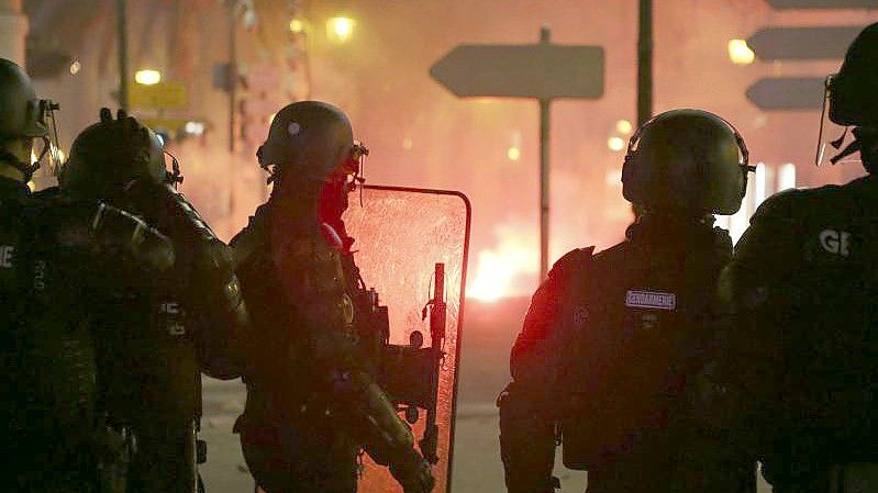 Französische Gendarmen stehen auf der Straße in Ajaccio auf Korsika, während es im Hintergrund brennt. Foto: Pascal Pochard-Casabianca/AFP/dpa