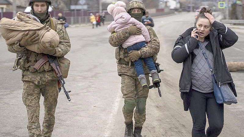 Ukrainische Soldaten in einem Außenbezirk von Kiew helfen einer fliehenden Familie bei der Suche nach einem Fahrzeug. Die US-Regierung geht davon aus, dass russische Soldaten in der Ukraine Kriegsverbrechen begehen. Foto: Emilio Morenatti/AP/dpa