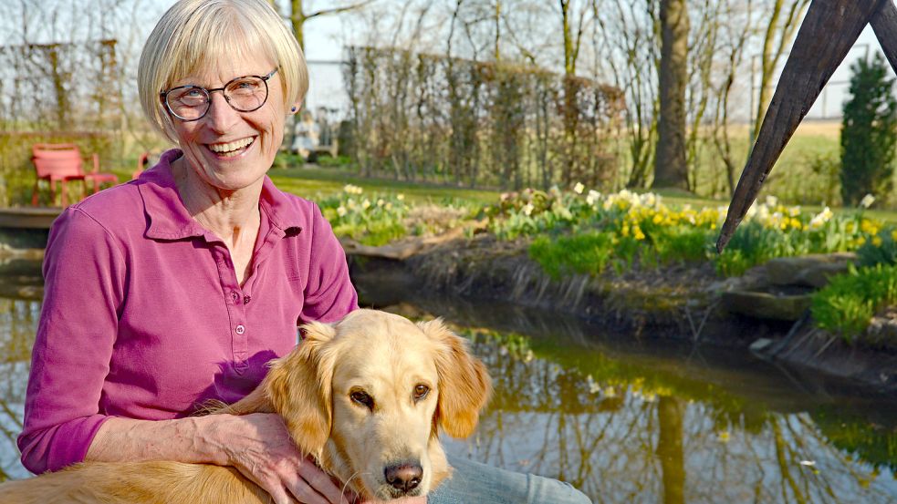 Meike Diddens genießt mit Hündin Emma die Sonne am Naturteich. Jetzt blühen dort Narzissen – später wird der Rand dicht bewachsen sein. Foto: Lüppen