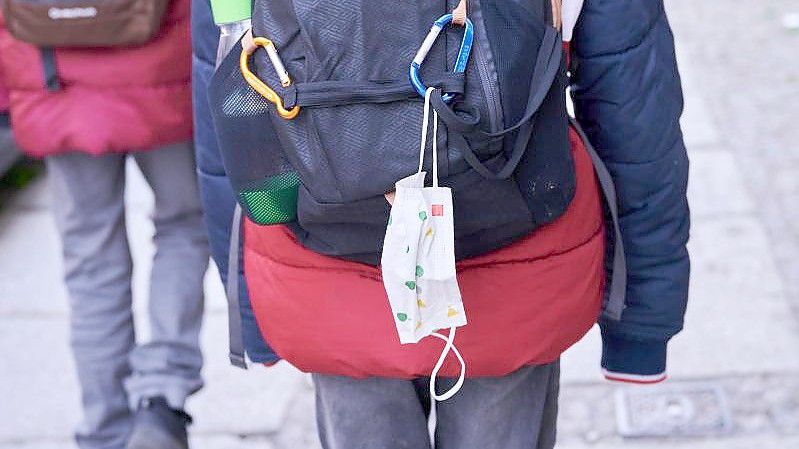 Eine Kindermaske hängt am Rucksack eines Schulkindes. Foto: Annette Riedl/dpa