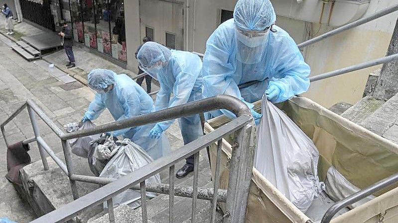 Hotelangestellte in Hongkong tragen Schutzkleidung und entsorgen Müll aus einem Hotel, das zur Isolation genutzt wird. Foto: Kin Cheung/AP/dpa