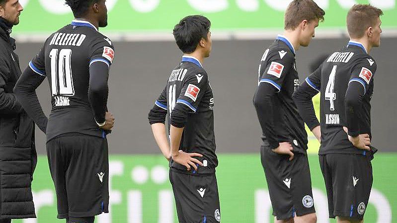 Nach dem 0:4 beim VfL Wolfsburg stehen die Spieler von Arminia Bielefeld mit gesenkten Köpfen auf dem Platz. Foto: Swen Pförtner/dpa