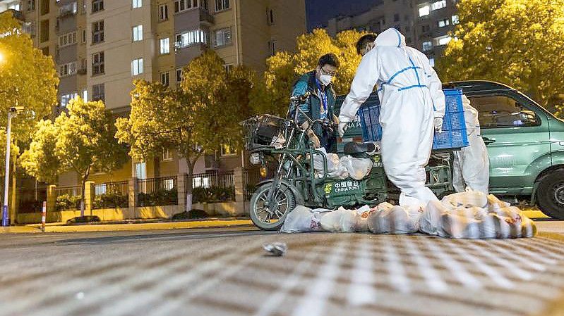 Lieferanten in Schutzanzügen tragen Tüten mit Lebensmitteln zum Tor einer Wohnanlage. Foto: Uncredited/AP/dpa