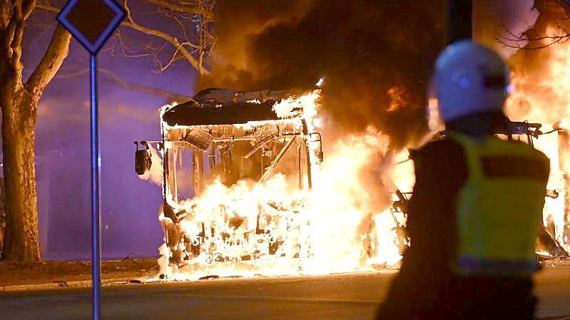 Bereitschaftspolizisten stehen vor einem brennenden Stadtbus. Foto: Johan Nilsson/TT NEWS AGENCY/AP/dpa