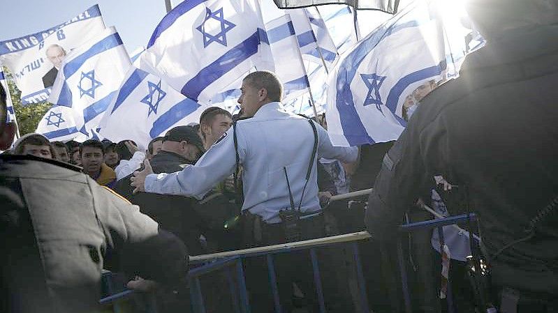 Ein israelischer Polizeibeamter steht vor rechten Aktivisten, die sich zu einem Flaggenmarsch in der Altstadt von Jerusalem versammelt haben. Foto: Ariel Schalit/AP/dpa