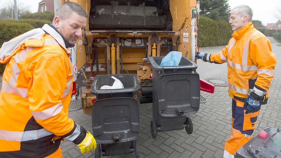 Die Emder Müllwerker Harri van der Werf (links) und Marco Rüst entleeren graue Restmülltonnen in einer Einfamilienhaussiedlung. In Teilen von Borssum und Barenburg gibt es nur noch große Container anstelle der einzelnen Tonnen. Foto: J. Doden/Archiv