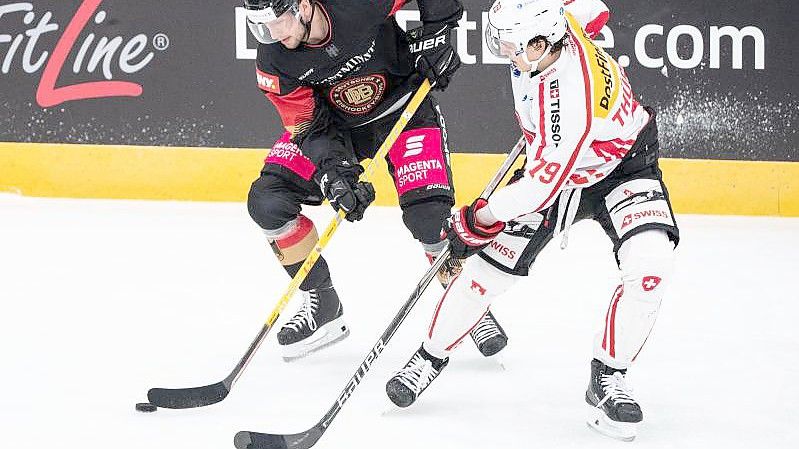 Tobias Eder (l) und der Schweizer Calvin Thürkauf im Zweikampf um den Puck. Foto: Matthias Balk/dpa