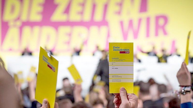 Delegierte halten beim ersten Präsenzparteitag der FDP nach dem Beginn von Corona die Stimmkarten hoch. Foto: Michael Kappeler/dpa