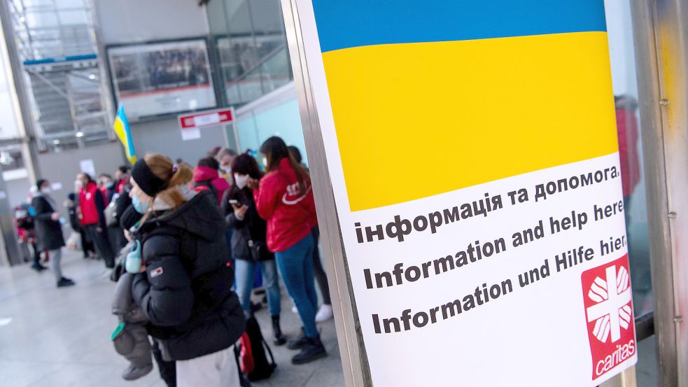 Ein Schild in den Farben der Ukraine mit der Aufschrift „Informationen und Hilfe hier“ ist am Hauptbahnhof Berlin zu sehen. Im Hintergrund werden Flüchtlinge aus der Ukraine nach ihrer Ankunft von Mitarbeitern der Caritas und freiwilligen Helfern empfangen. Foto: DPA