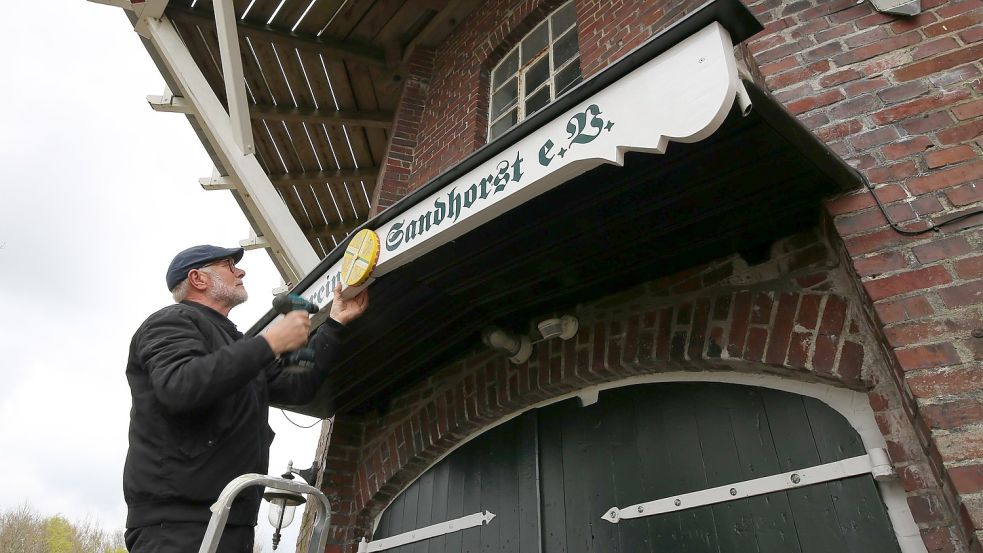 Mühlenwart Gerhard Poppen montiert die Verzierung auf dem neuen Vereinsschild am Eingang der Mühle. Foto: Böning