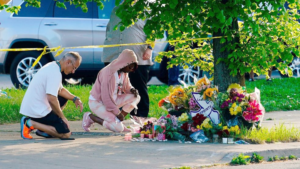 Menschen knien vor Blumen, um den Opfern tödlicher Schüsse in einem Supermarkt in Buffalo die letzte Ehre zu erweisen. Foto: Matt Rourke/AP/dpa