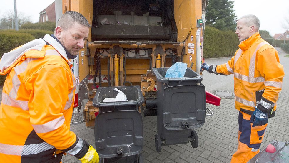 Die Emder Müllwerker Harri van der Werf (links) und Marco Rüst entleeren graue Restmülltonnen in einer Einfamilienhaussiedlung. Viele Menschen werfen ihren Biomüll in die Restmülltonne. Das ist teuer und schlechter für die Umwelt. Foto: J. Doden/Archiv