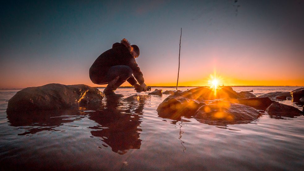 Thomas Heyen kniet auf einer Buhne am Emsufer, die Kamera möglichst nah am Wasser, den Sonnenuntergang im Blick. Foto: Cordsen