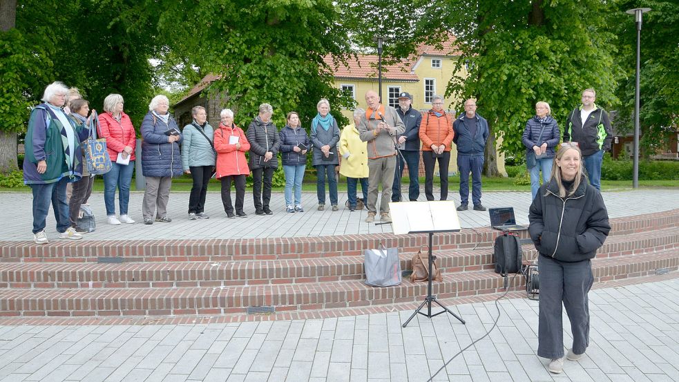 Wegen kriegsbedingter Lieferengpässe konnten die endgültigen Großplakate noch nicht am Neuen Weg zwischen Emden und Groß Midlum aufgestellt werden. Darum wurde die Aktion jetzt erst einmal provisorisch auf dem Pewsumer Marktplatz gestartet. Das Bild zeigt LAK-Mitglieder, die bei der Veranstaltung sangen. Am Mikrofon steht der LAK-Vorsitzende Hero-Georg Boomgaarden, vorne im Bild ist die LAK-Geschäftsführerin Christine Schmidt zu sehen.