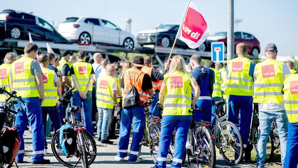 Mitarbeiter der Hafenbetriebe streiken am Donnerstag vor dem Tor zum Hafengelände im Seehafen Emden, während ein Autotransporter die Einfahrt passiert. Foto: Dittrich/DPA