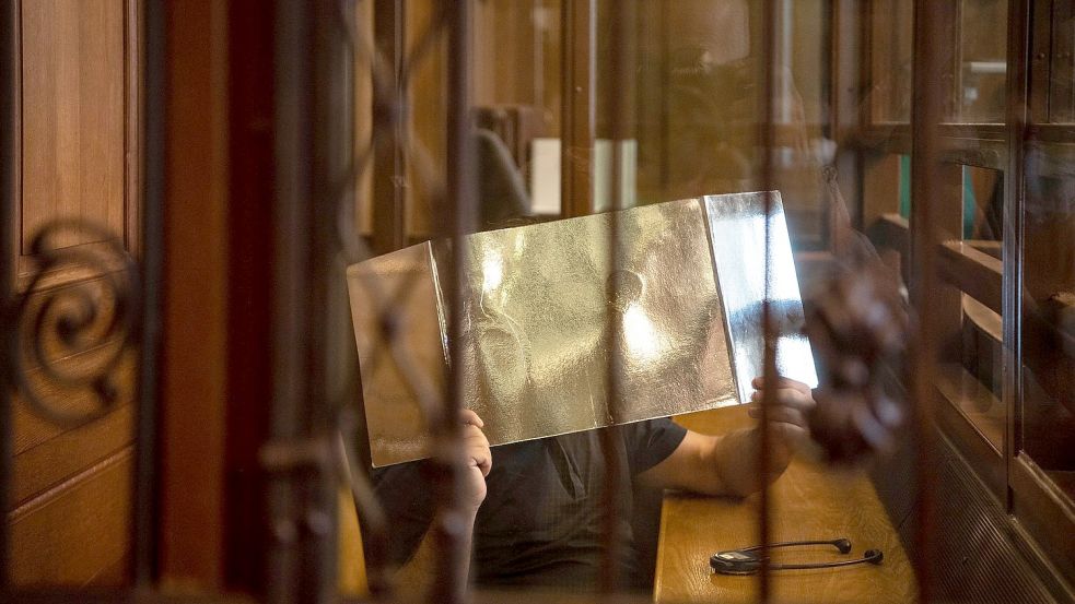 Der Angeklagte hält sich in einem Gerichtssaal eine Pappe vor sein Gesicht. Foto: Paul Zinken/dpa