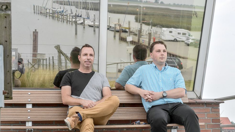 Nachbarn unter sich: Rolf Bolinius (links) und Christopher Krull sitzen vor dem Gebäude des neuen Siels. In den Fenstern spiegelt sich der Hafen. Foto: Ortgies
