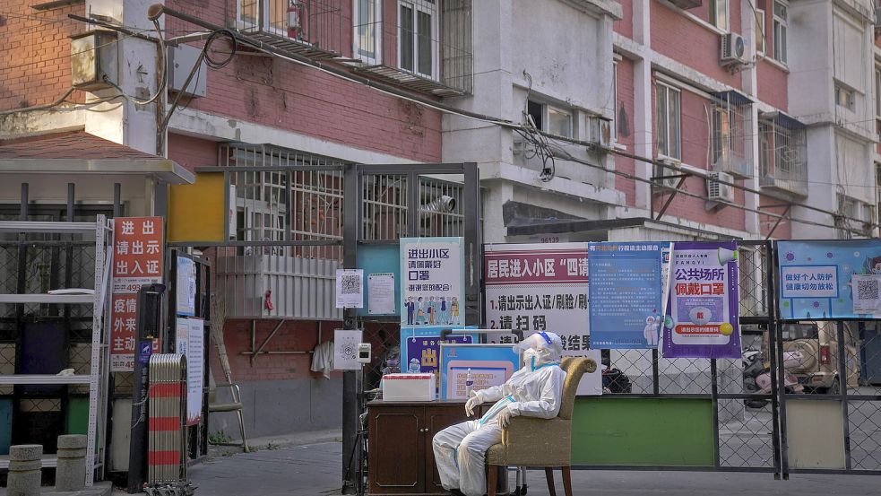 Ein Wachmann im Schutzanzug sitzt an einem Eingangstor zu einem Wohnviertel in Peking. Foto: Wong/AP/DPA