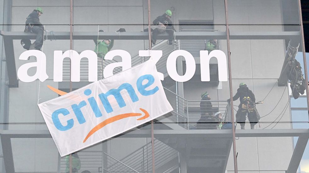 Greenpeace-Aktive hängen während der Rabattaktion Black Friday ein Plakat gegen die Ressourcenverschwendung des Online-Versandhändlers Amazon an dessen Gebäude in München auf. Foto: Felix Hörhager/dpa