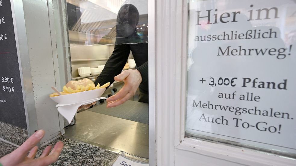 Eine Hand hält an einem Imbiss einen Mehrwegteller mit Pommes und einem Burger. Kunden haben künftig ein Anrecht darauf, ihre To-Go-Speisen und -Getränke in einer Mehrwegverpackung zu bekommen. Foto: Weißbrod/dpa