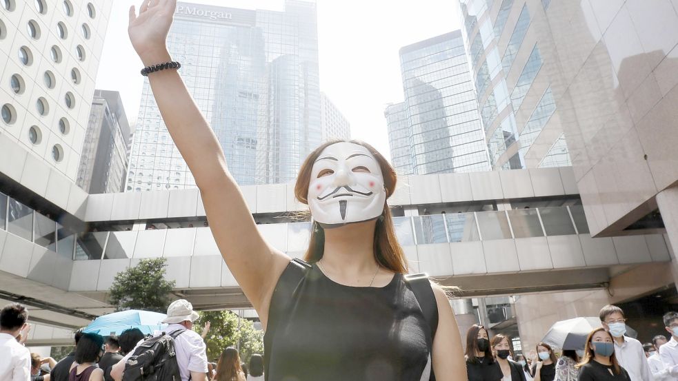 Mit der Maske für das Recht: Eine maskierte Frau steht mit erhobener Hand auf der Straße. Demonstranten wehren sich gegen ein Notstandsgesetz der Regierung, das den Demonstranten das Tragen von Gesichtsmasken verbietet. Foto: kyodo