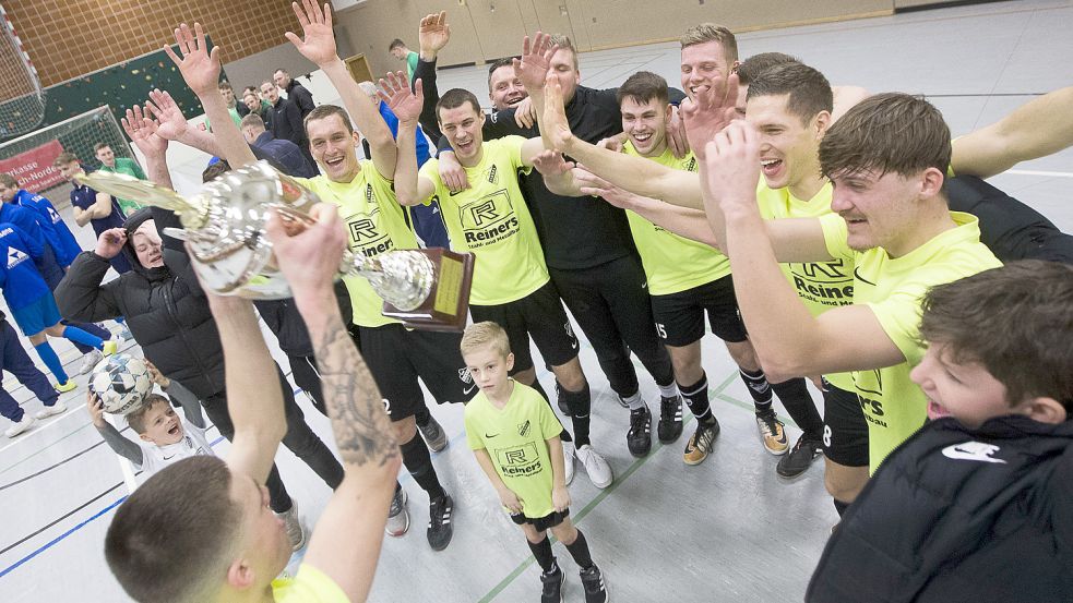 Nächster Pokal für die Vereinsvitrine: Lukas Koch stemmt den Wanderpokal vor seinen jubelnden Mitspielern in die Luft. Im vierten Turnier feierte der Landesligist den vierten Sieg. Foto: Doden/Emden