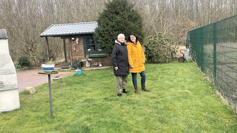 Gerta Schinzel und ihre Tochter Sabine Janßen stehen an der Grenze des Grundstücks der Seniorin. Rechts von ihnen soll der neue Weg in den Stadtwald (im Hintergrund) verlaufen. Ganz rechts ist der Zaun zu sehen, der ein Regenrückhaltebecken umgibt. Foto: H. Müller