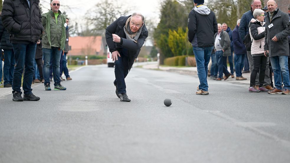 Stephan Weil, Ministerpräsident von Niedersachsen, wirft eine Boßelkugel aus Pockholz über die Straße. Foto: Lars Klemmer/dpa