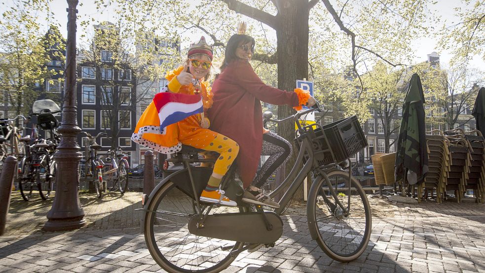 Eine Mutter und ihre Tochter, die ein orangefarbenes Königsgewand mit der niederländischen Flagge trägt, fahren am Königstag 2021 mit dem Rad. Foto: Dejong/AP/dpa