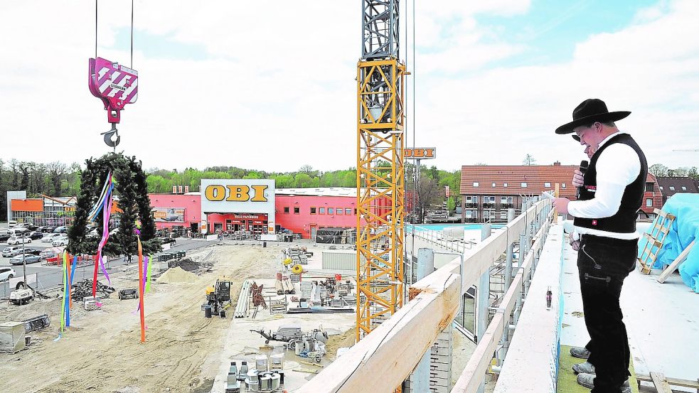 Während der 20-jährige Zimmermann Jannes Gödiker vom Bauunternehmen Schulte auf dem Dach des Ems-Center-Rohbaus den Richtspruch vorlas, wurde mithilfe eines Krans der Richtkranz emporgehoben.Foto: Schade