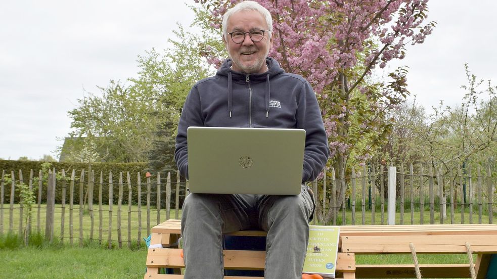 Manfred Reuter sitzt mit Laptop und Buch in seinem Garten. Foto: Hoppe