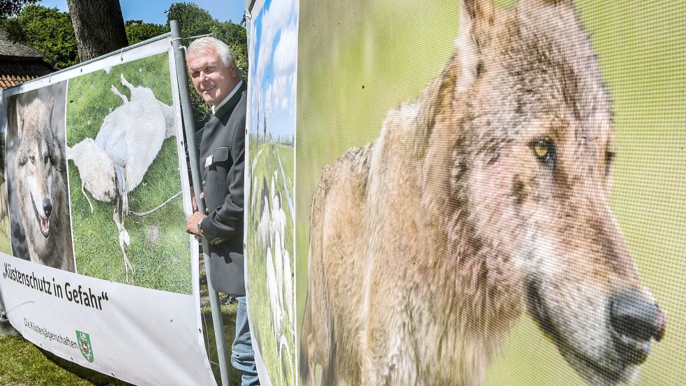 Gernold Lengert posiert zwischen zwei Bannern, mit denen die Jägerschaft auf Gefahren für den Küstenschutz durch den Wolf hinweist. Foto: Ortgies