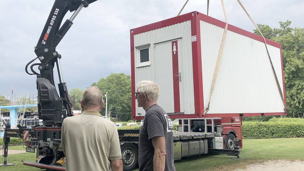 Die ersten Container für den Notbetrieb sind schon da: Friedhelm Jakobs (rechts), Technikschef des Van-Ameren-Bades, und sein Vorgänger Peter Kurzak verfolgen, wie der erste von zwei Toilettencontainern auf dem Gelände des Freibads abgeladen wird. Foto: H. Müller