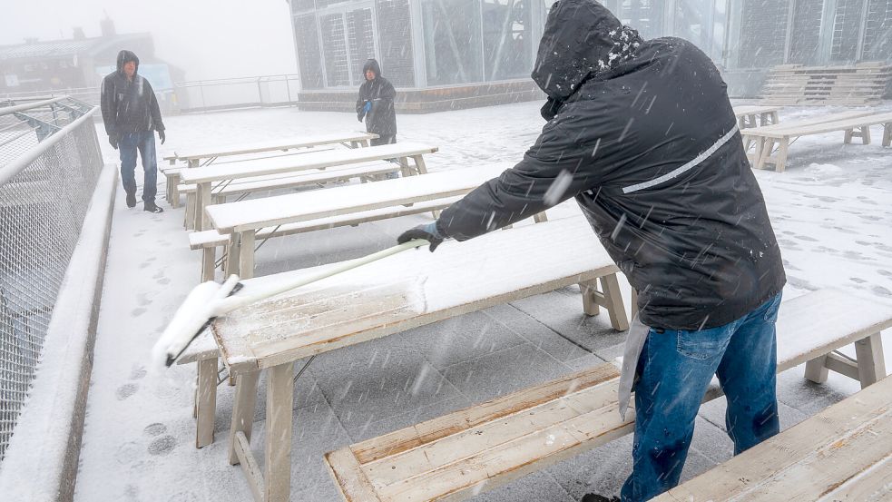 Ein Mann entfernt bei Schneetreiben auf der Zugspitze den Schnee von den Tischen auf der verschneiten Aussichtsplattform. Foto: dpa/Peter Kneffel