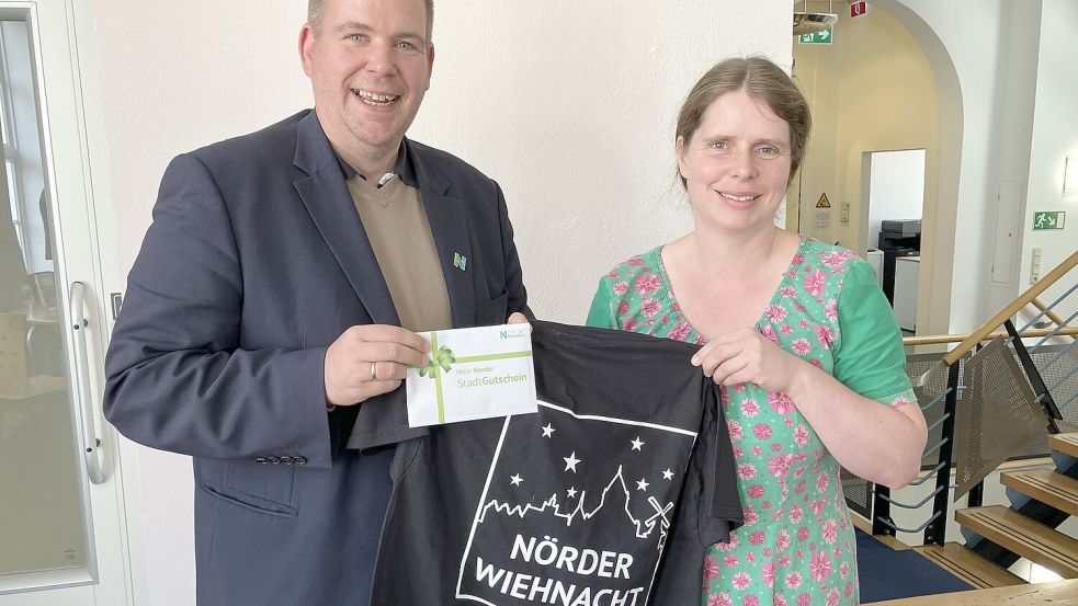 Bürgermeister Florian Eiben überreichte Silvia Ubben aus Aurich einen Stadtgutschein im Wert von 100 Euro und ein T-Shirt mit dem neuen Logo des Norder Weihnachtsmarktes. Foto: Rebecca Kresse