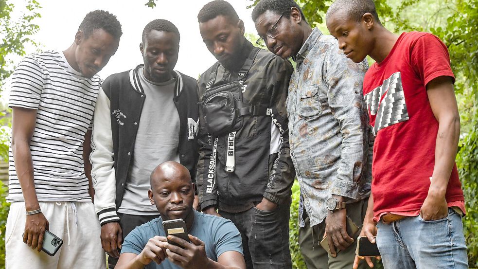 Das Smartphone ist das wichtigste Informationsmittel für Menschen aus Westafrika, um zu erfahren, was in ihren Heimatstaaten los ist. Ali Koné (hockend) diskutiert mit Vereinsmitgliedern über die politische Lage. Foto: Ortgies