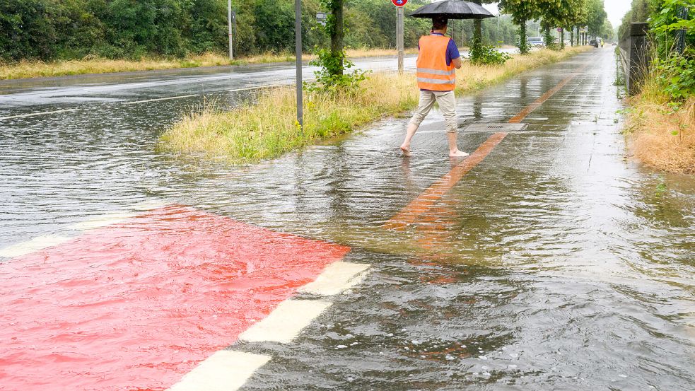 Im Juni in Hannover: Ein Mann geht barfuss durch das Wasser an der überfluteten Hermesallee am Messegelände. Foto: Stratenschulte/dpa