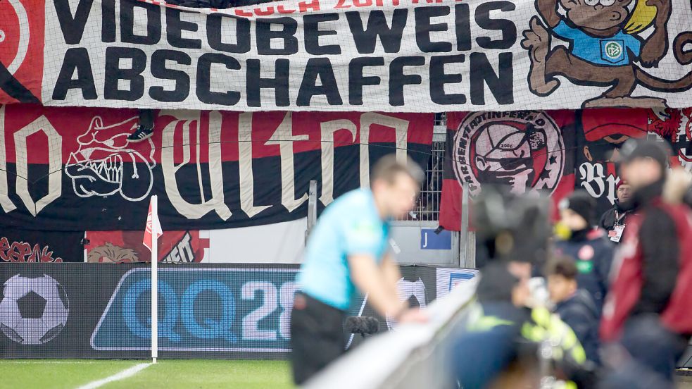 Während Schiedsrichter Patrick Ittrich am VAR-Monitor steht, protestieren hinter ihm Leverkusener Fans gegen den Einsatz der Technik. Foto: imago/Kessler-Sportfotografie
