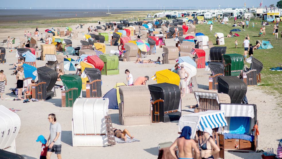 Touristen sitzen bei sommerlichen Temperaturen am Strand von Dangast. Foto: Dittrich/dpa