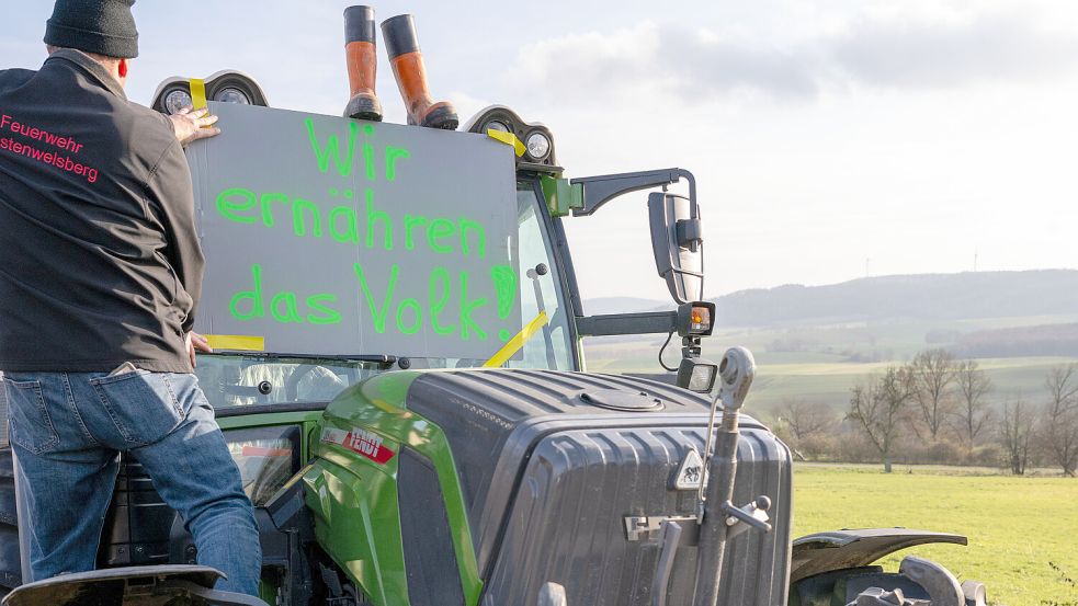 Ein Landwirt befestigt ein Protestschild an seinem Schlepper. Deutsche Bauern laufen Sturm gegen eine angekündigte Streichung der Agrardiesel-Subvention und der Kfz-Steuerbefreiung für die Landwirtschaft. Zahlreiche Protest-Aktionen sind geplant. Foto: Pia Bayer/dpa