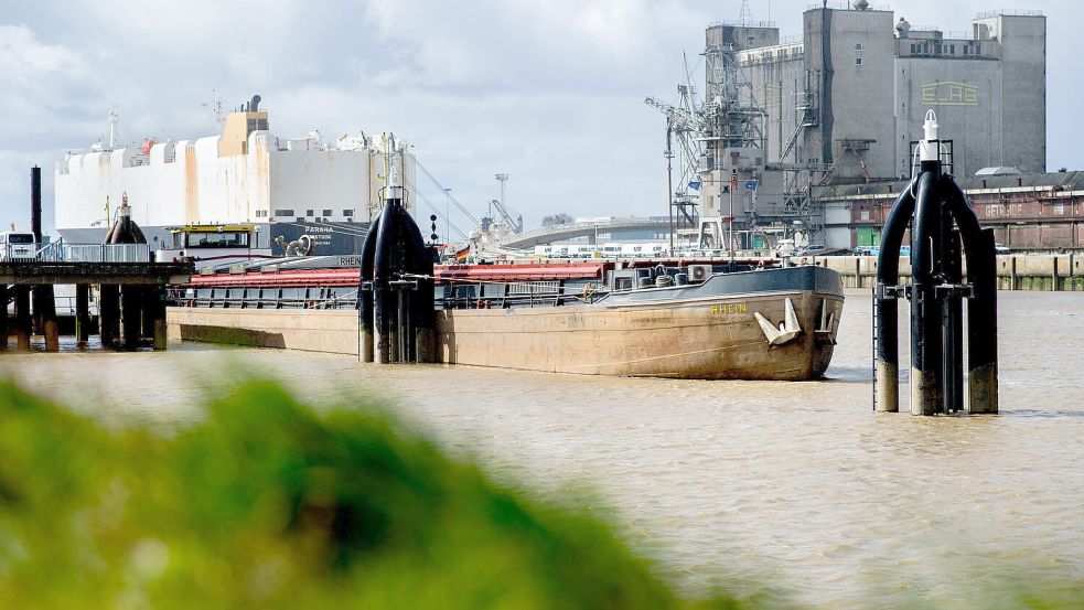 Blick in den Emder Hafen: Ein Binnenschiff liegt an einem Anleger im Außenhafen, während im Hintergrund ein Autotransporter am Autoport an einer Kaimauer liegt. Foto: Dittrich/DPA