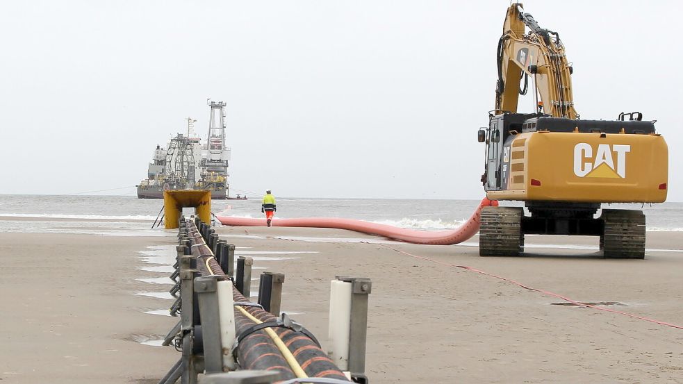 Am Strand von Norderney verschwindet ein Stromkabel im Meer. Im Hintergrund ein Verlegeschiff, von dem aus der Kabelstrang auf den Meeresboden hinabgelassen wird, bis hinaus zu einem Windpark. Foto: Oltmanns