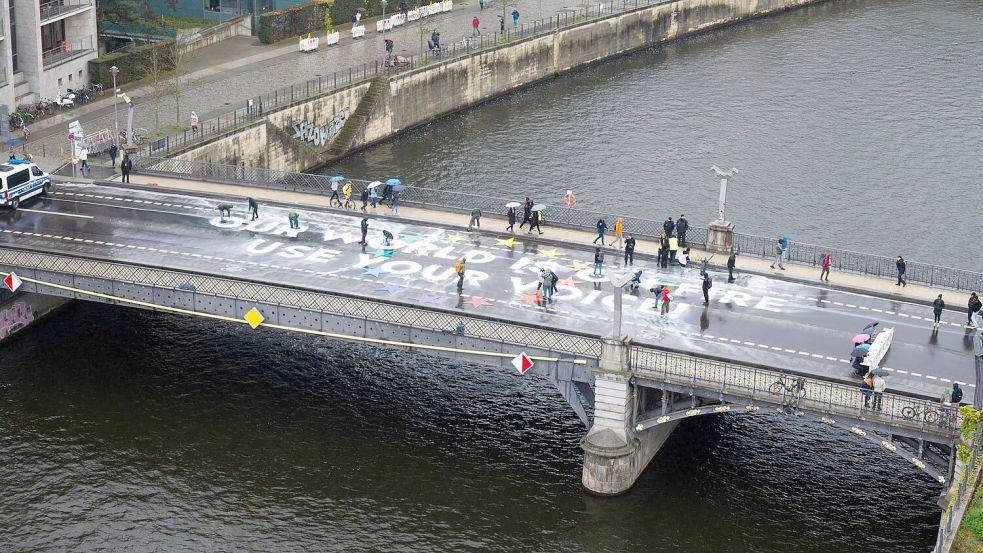 Klimaaktivisten der Bewegung Fridays for Future malen auf der Marschallbrücke in Berlin den Schriftzug „Our world is on fire - use your voice!“. Foto: Christophe Gateau/dpa