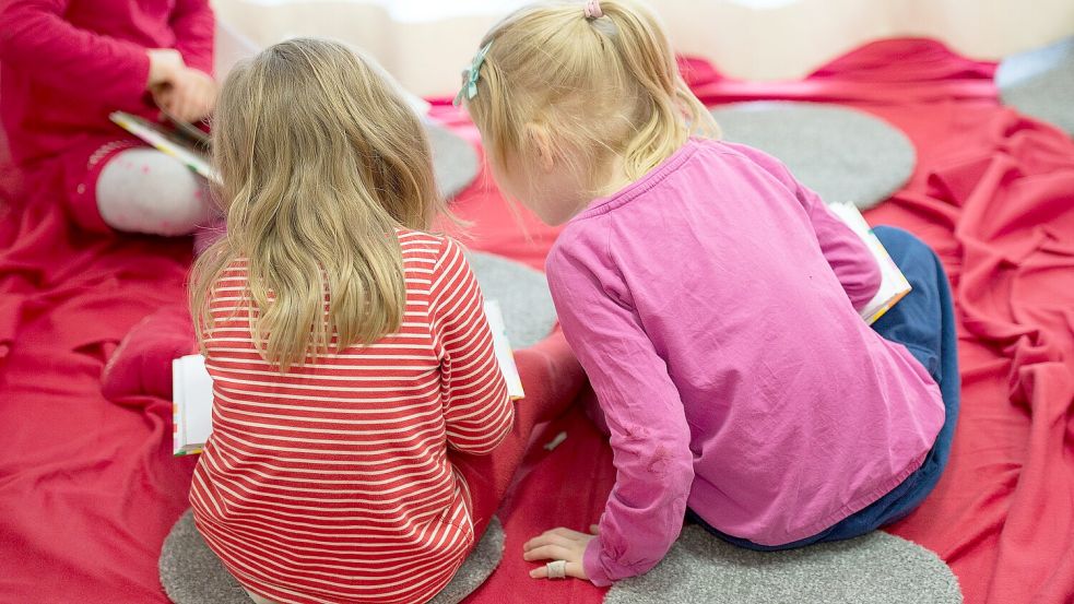 Zwei Mädchen lesen in einer Kita in einem Buch. Foto: DPA