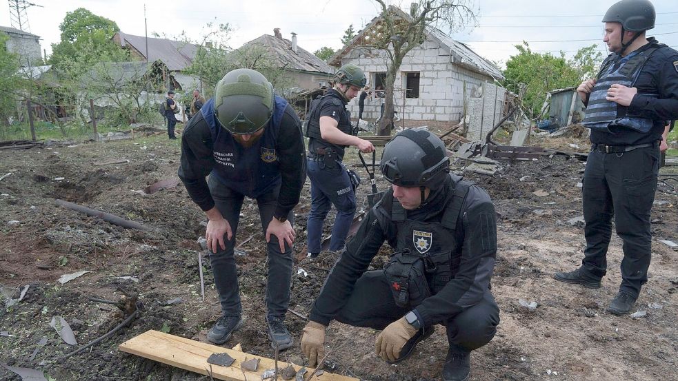 Ein ukrainischer Polizeibeamter und ein Staatsanwalt für Kriegsverbrechen inspizieren Bruchstücke einer Gleitbombe vor einem beschädigten Haus nach einem russischen Luftangriff auf ein Wohnviertel. Foto: Evgeniy Maloletka/AP/dpa