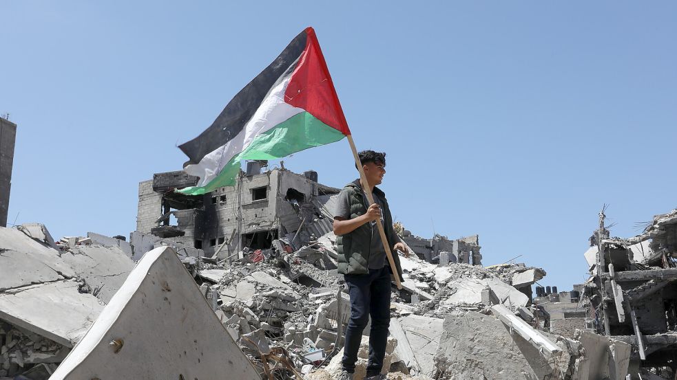 Ein Palästinenser hält die palästinensische Fahne in der Hand, während er auf Trümmern nach israelischem Beschuss steht. Foto: dpa/Abed Rahim Khatib