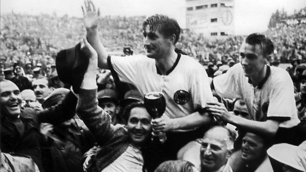 Ein historischer Moment: Der deutsche Stürmer und Kapitän Fritz Walter (Mitte, oben) und sein Lauterer Teamgefährte Horst Eckel (rechts) werden nach dem Triumph im Fußball-WM-Finale am 4. Juli 1954 im Berner Wankdorfstadion von begeisterten Anhängern vom Spielfeld getragen. Fritz Walter hält den Jules-Rimet-Pokal in der Hand, den er mit seiner Mannschaft gewinnt. Die deutsche Fußballnationalmannschaft besiegt Ungarn mit 3:2. Foto: DPA/Archiv