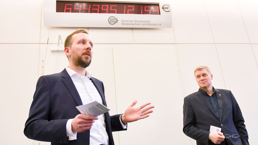 Jan Vermöhlen (l.) vom Bund der Steuerzahler, und Ulf Thiele, finanzpolitischer Sprecher der CDU-Landtagsfraktion vor der niedersächsischen Schuldenuhr. Im Jahr 2025 steigt diese sekündlich um 48,06 Euro pro Sekunde. Foto: dpa/Ella Wenzel